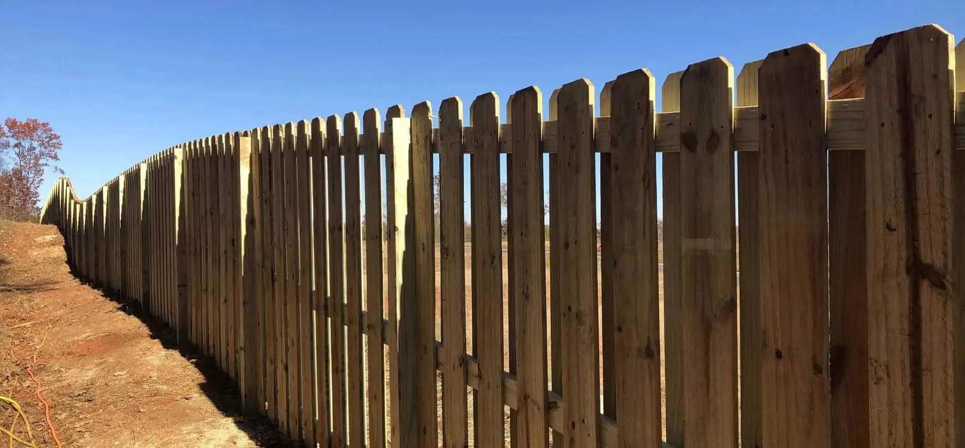 Wooden fence curves along a dirt path under a clear blue sky.