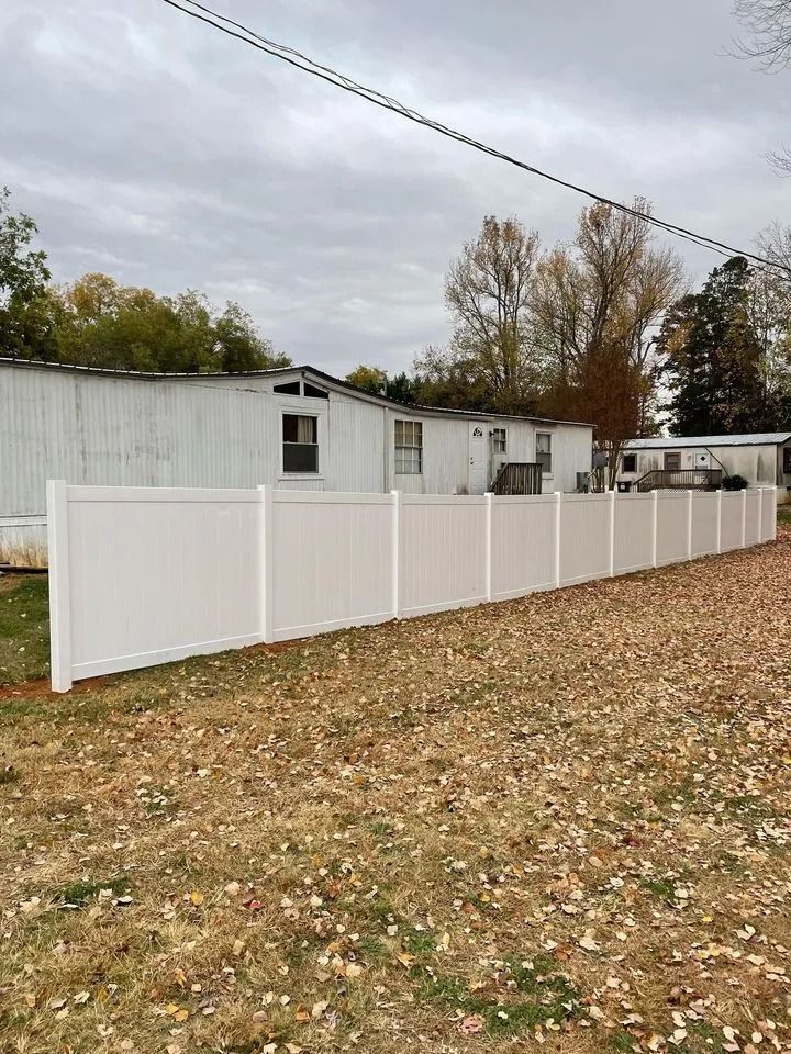White vinyl fence in front of a white mobile home on a cloudy day.
