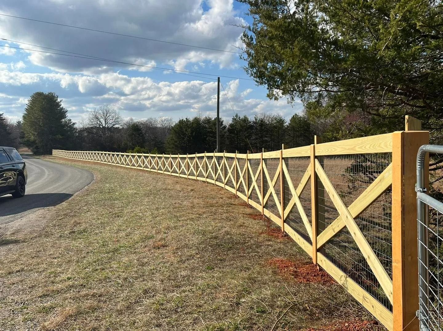 A long wooden fence with X-shaped crossbeams curves along a road.