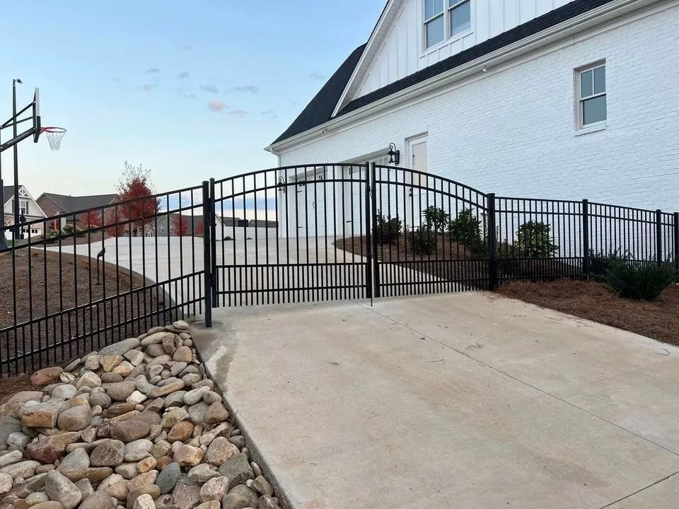 Black metal fence and gate encloses a driveway in front of a white brick house.