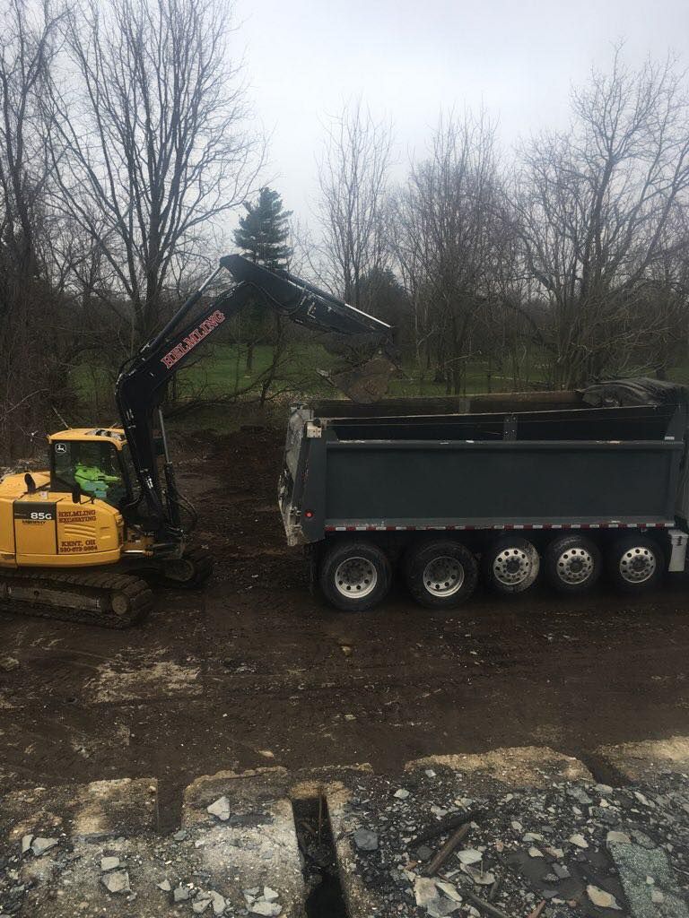 A dump truck is being loaded with dirt by a crane.