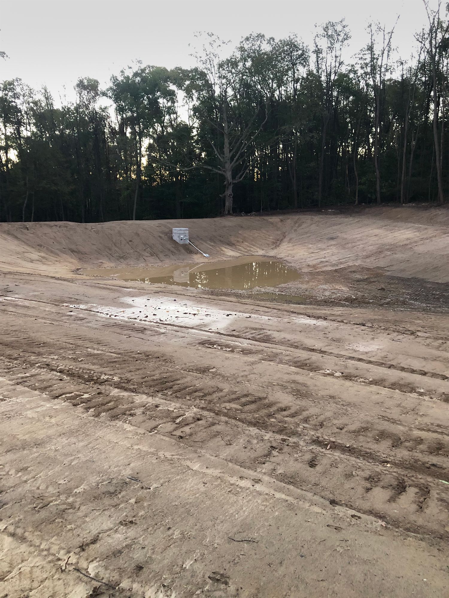 A muddy field with trees in the background and a puddle in the middle
