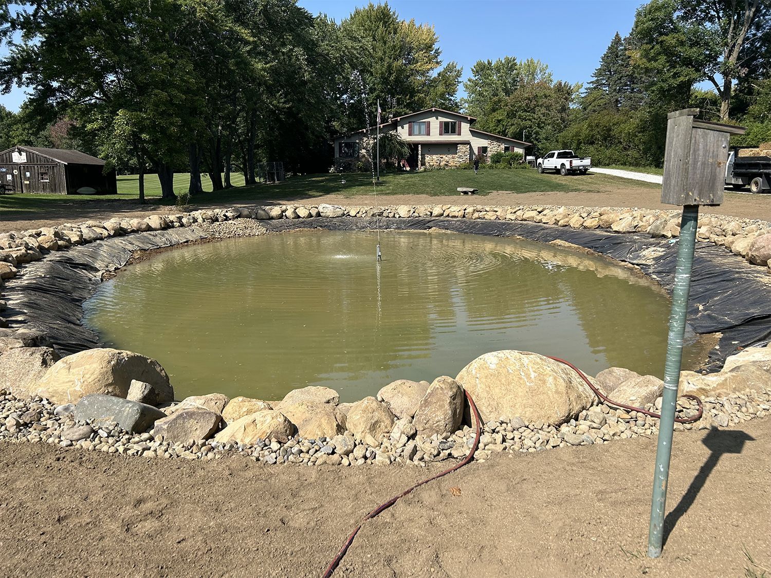 A large pond surrounded by rocks and dirt with a house in the background.