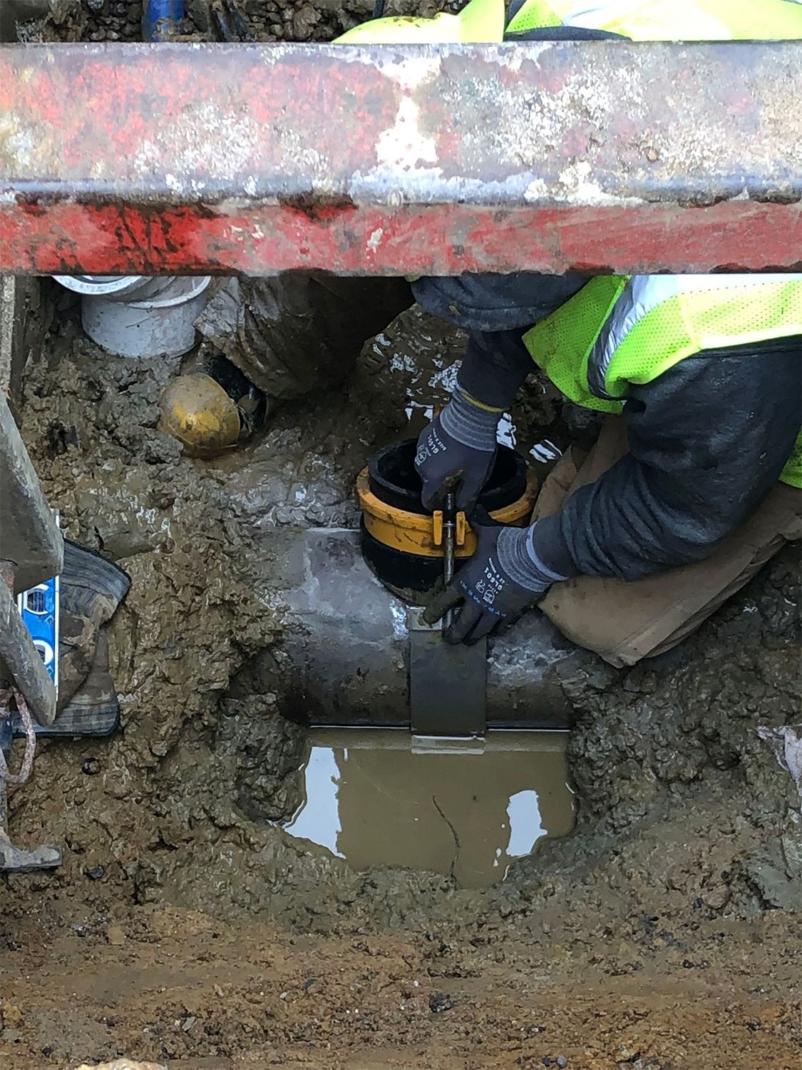 A man is working on a pipe in the mud.