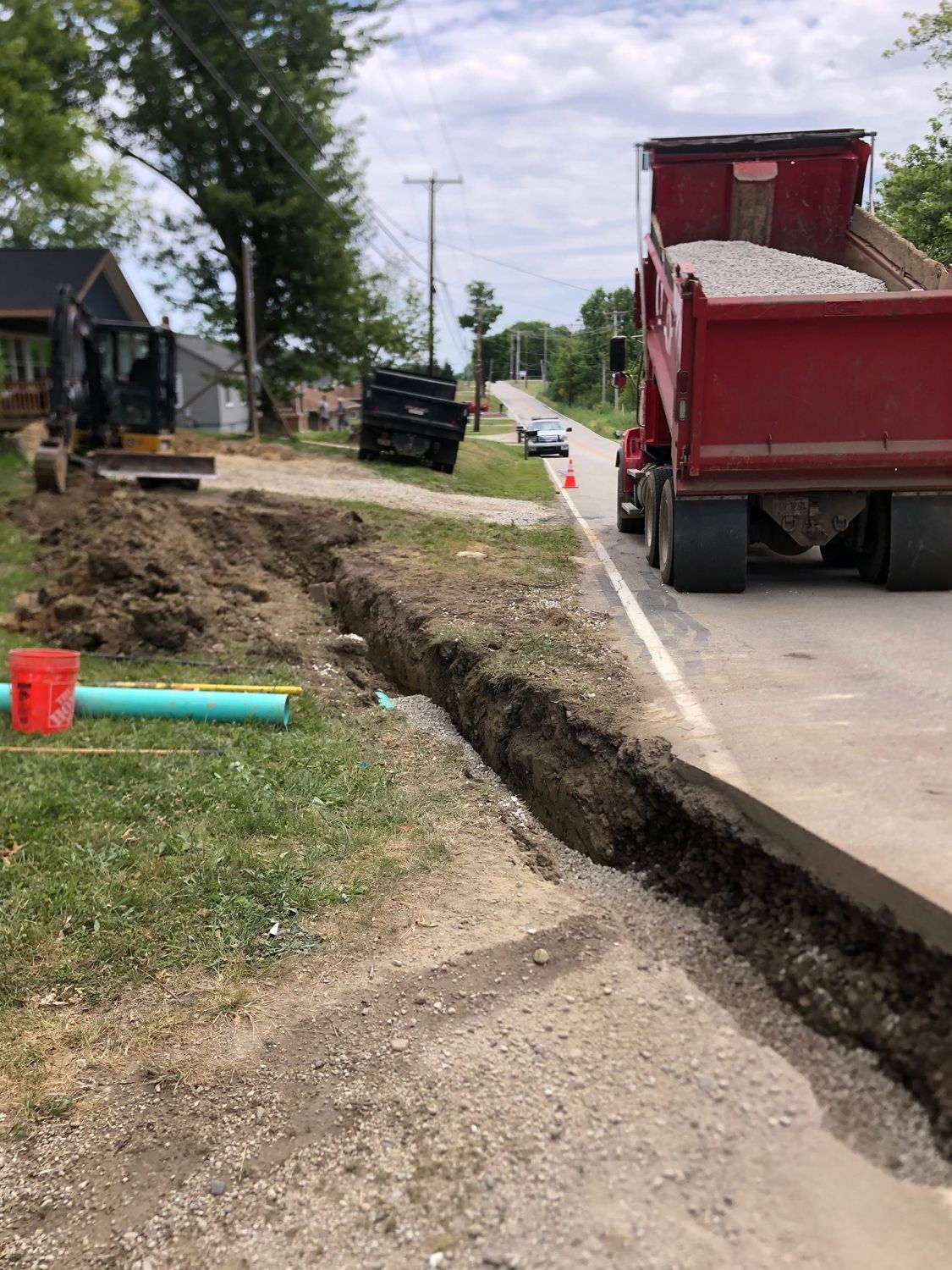 A red dump truck is driving down a street next to a trench.