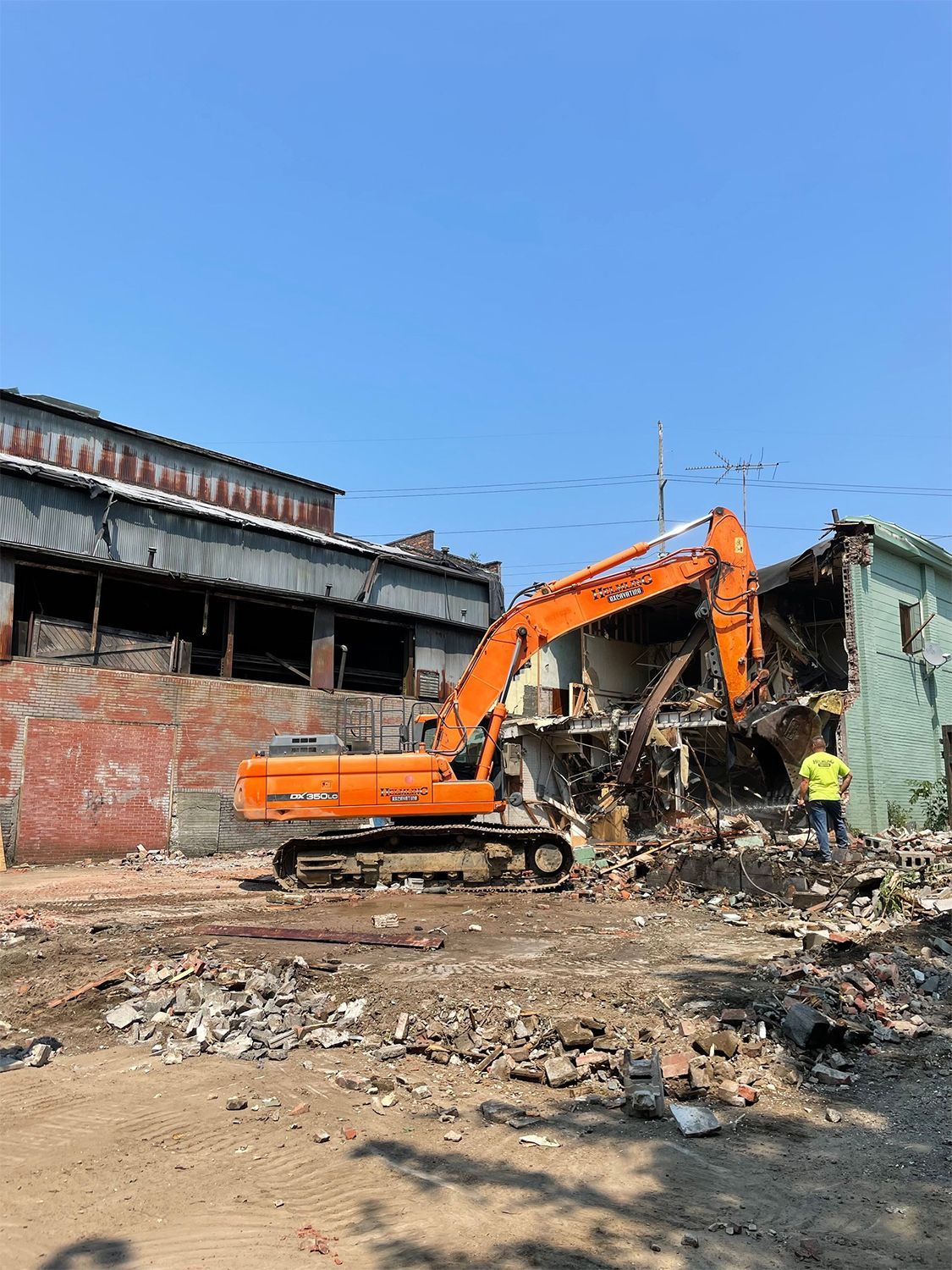 A large orange excavator is demolishing a building.