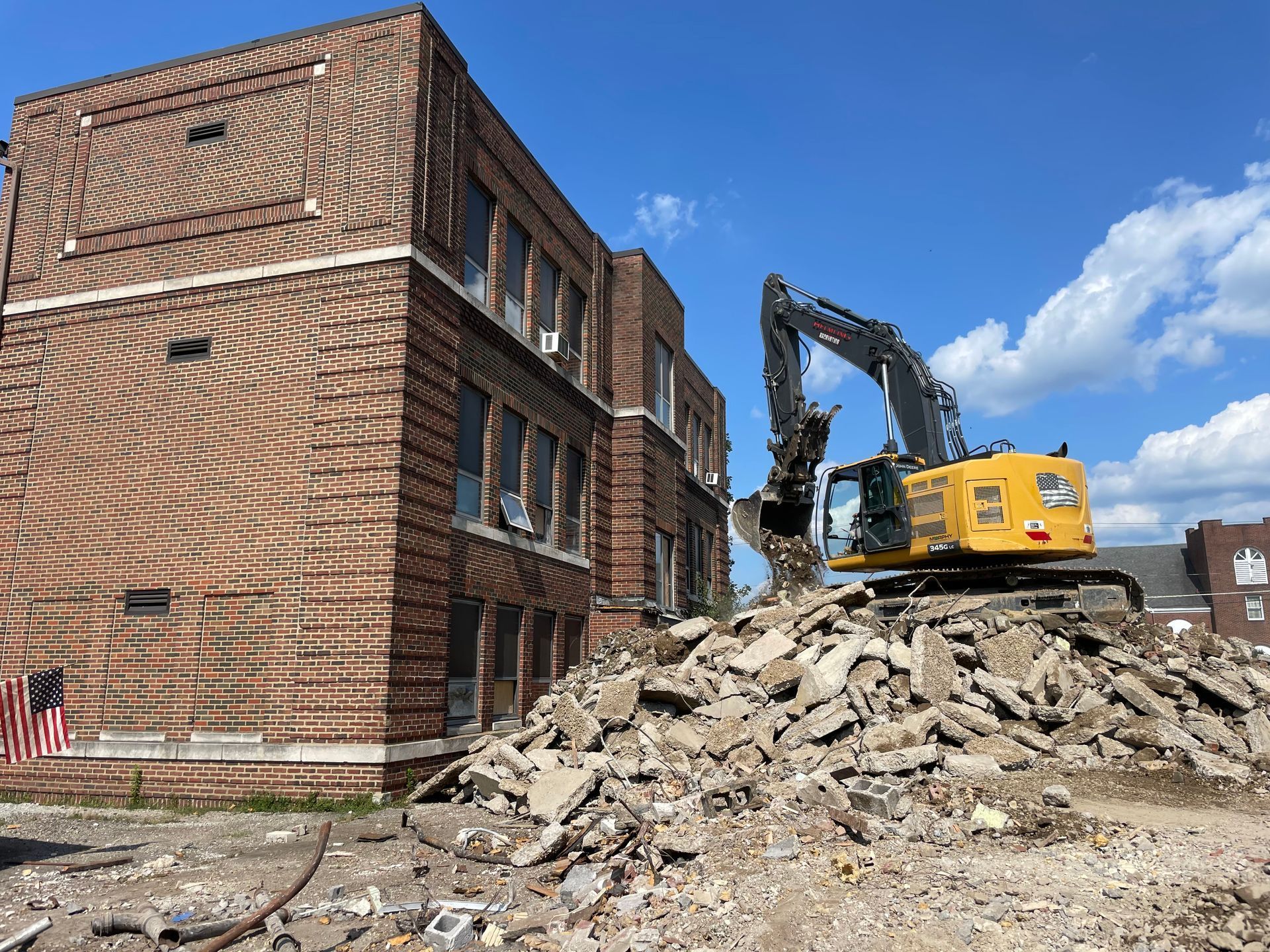 A large yellow excavator is demolishing a brick building.