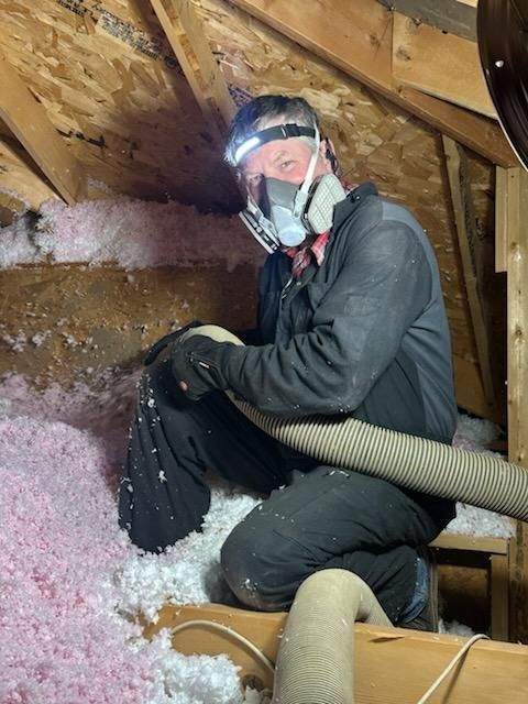 Person in an attic wearing a respirator and headlamp, installing pink insulation.