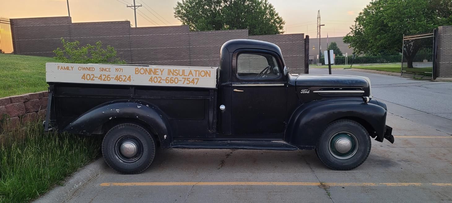 Black vintage pickup truck parked in front of a brick wall. The truck bed has text.