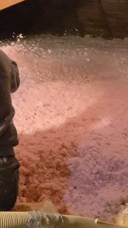 Person spraying pink insulation into an attic space.