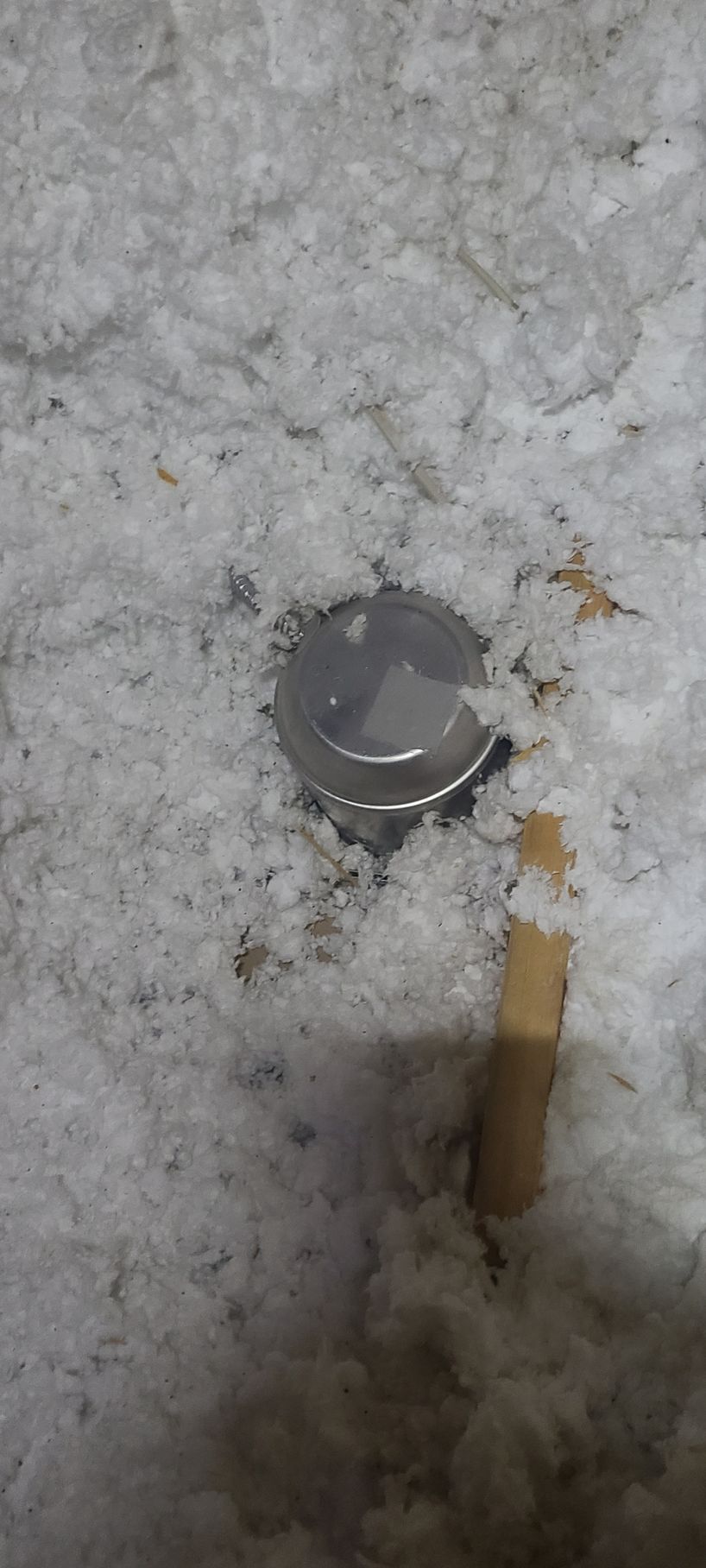 A metal object surrounded by white insulation, and a wooden stick partially visible.