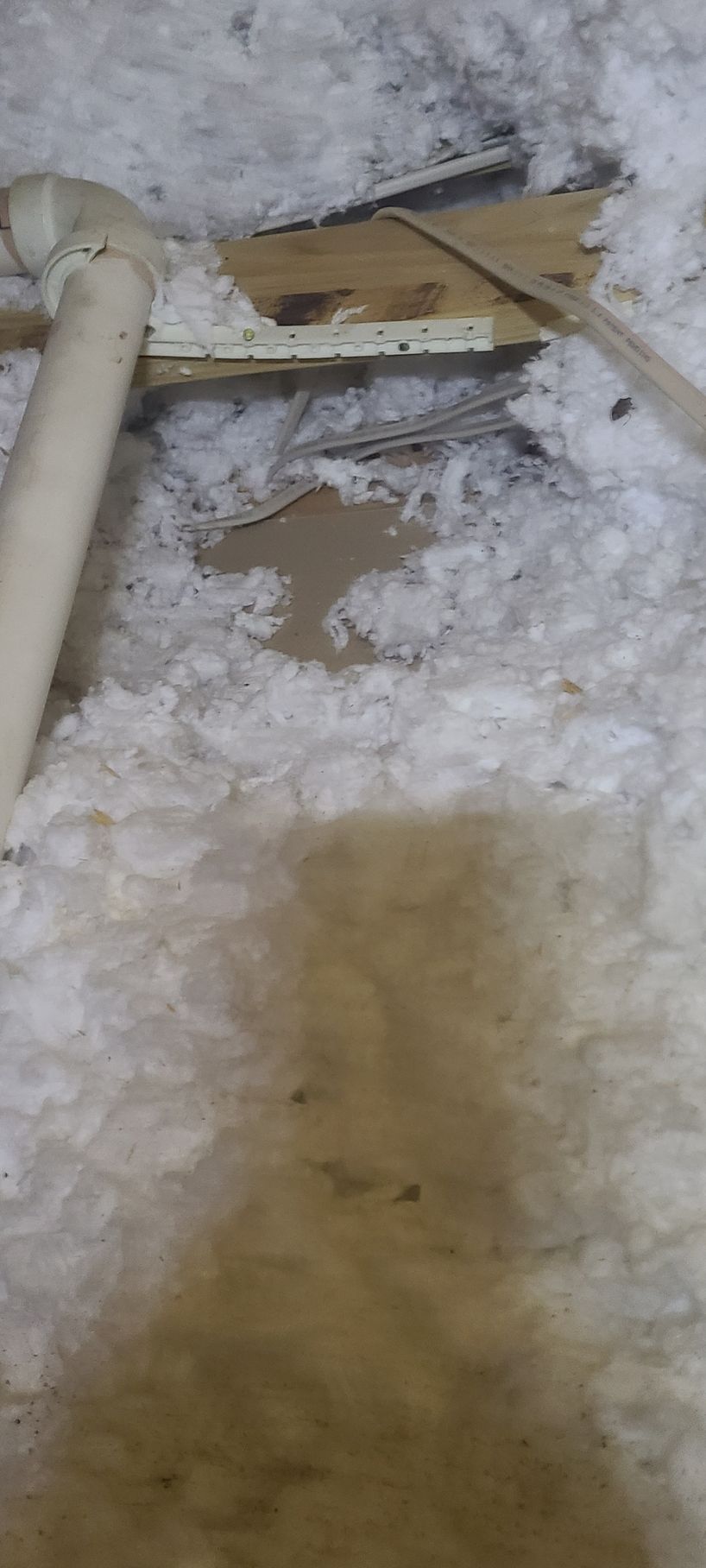 Water damage in an attic, soaked insulation and a broken wooden board, light brown tones.