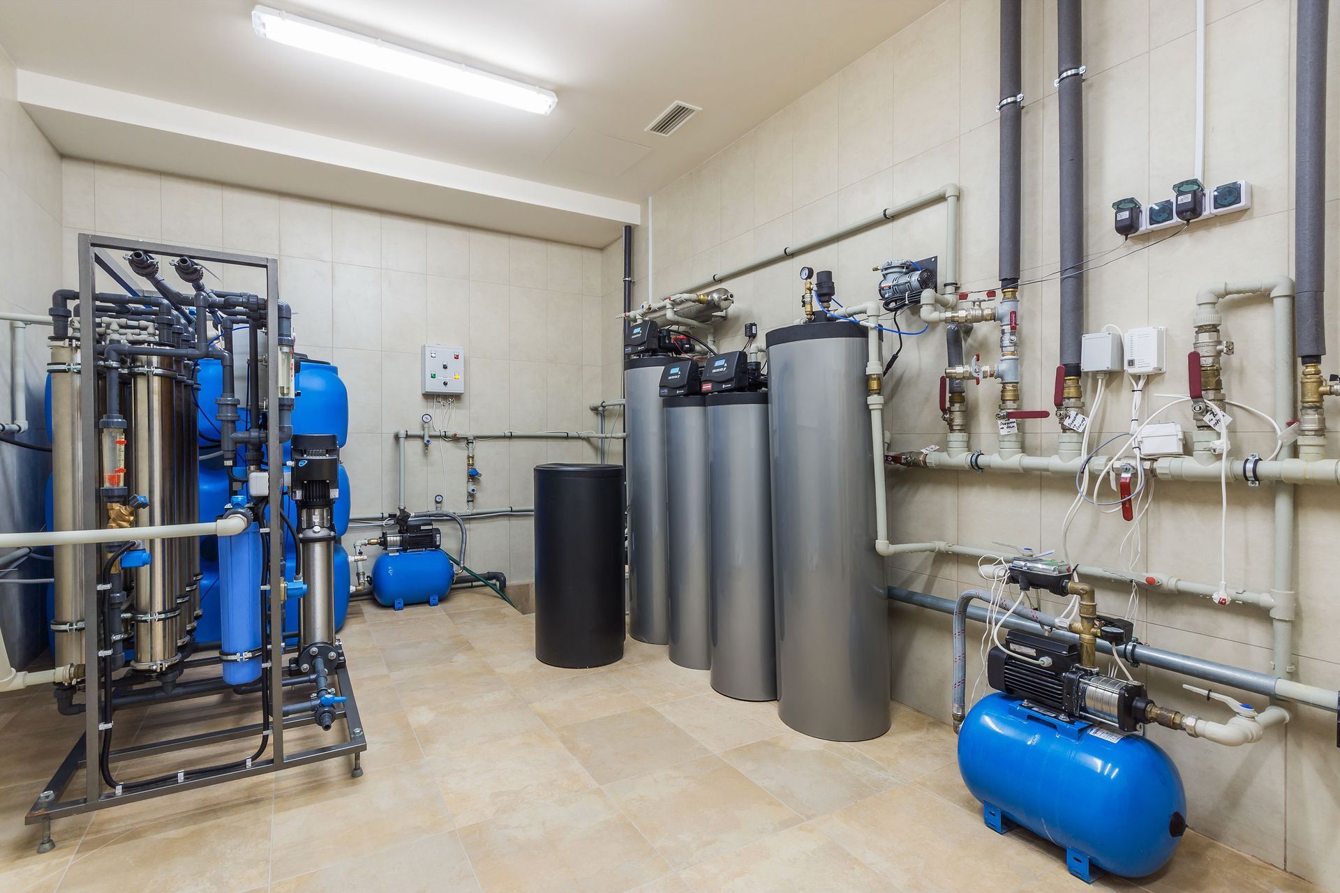 Water treatment equipment in a utility room. Blue tanks, silver cylinders, and piping are visible.