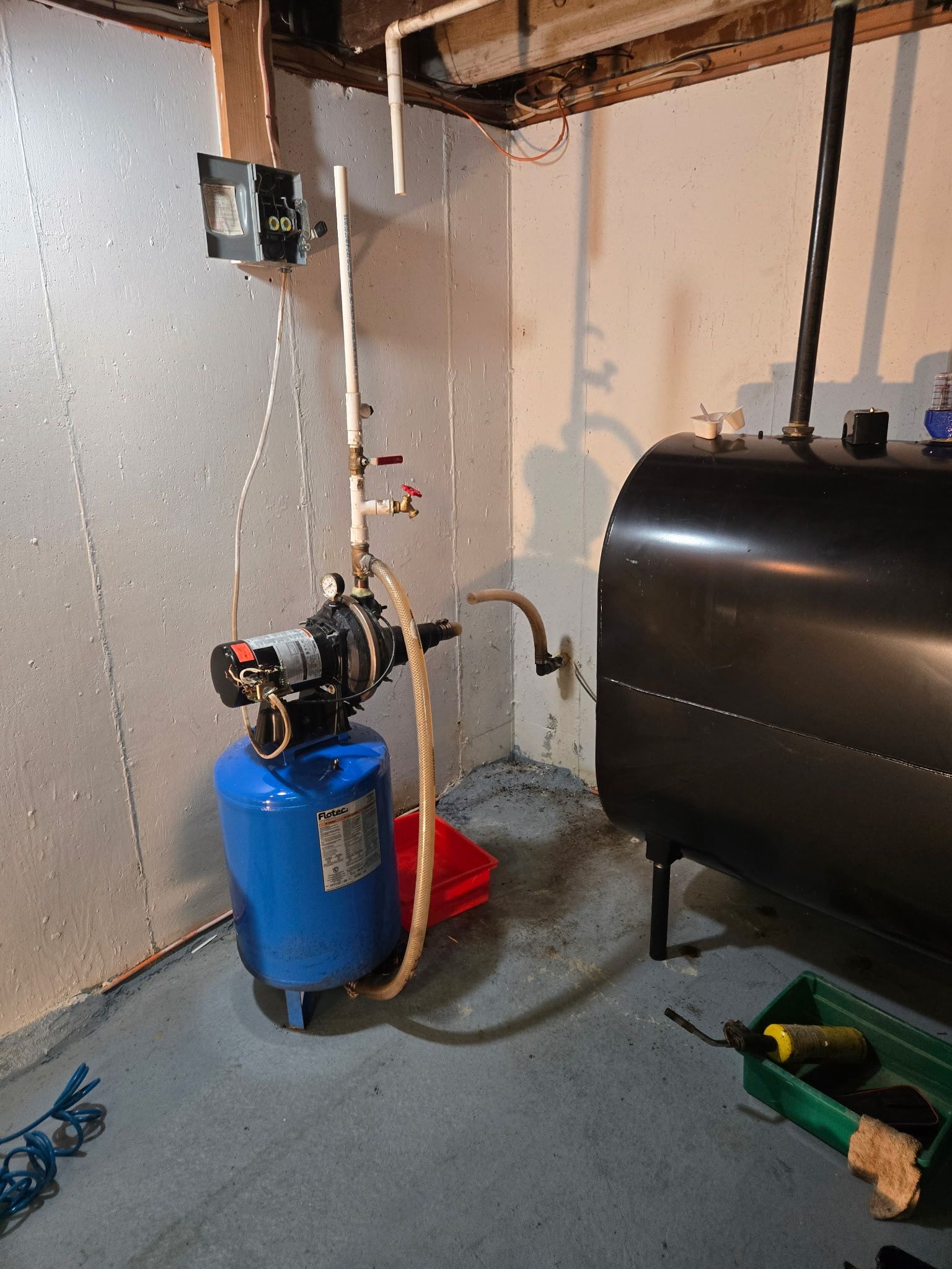 Basement with blue water tank, pump, and black oil tank against a wall. Plumbing visible.