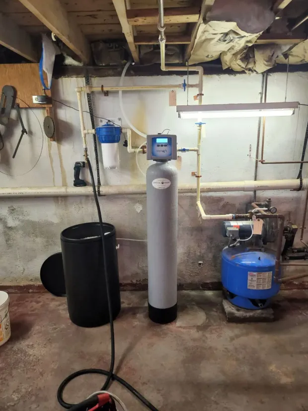 Basement water filtration system with a blue tank, gray softener, and white filter.