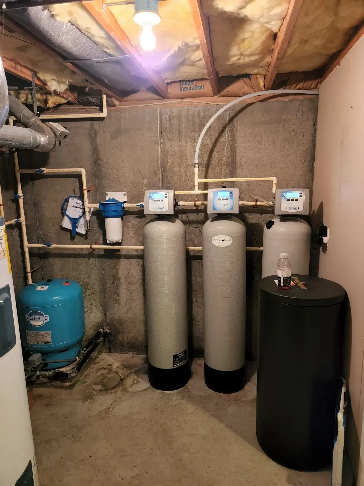 Water treatment system in a basement; includes tanks, filters, pressure tank, pipes, and control panels.