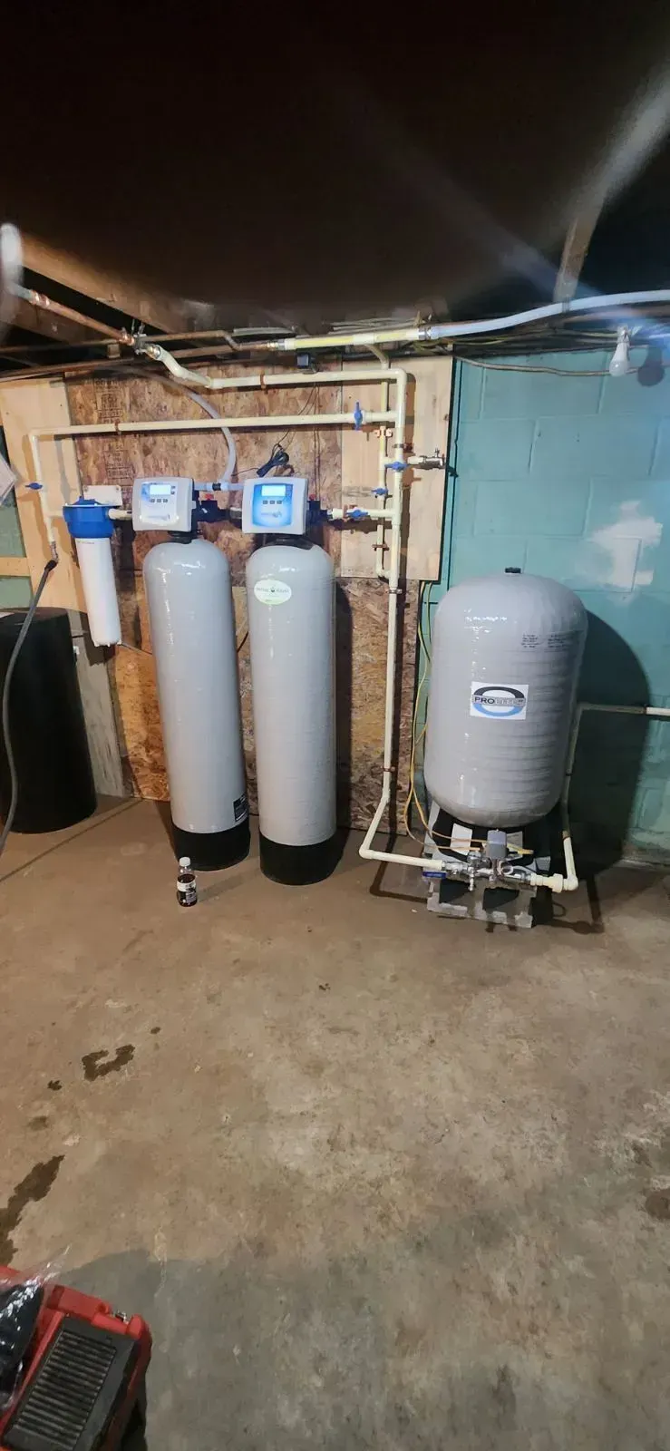 Water filtration and pressure system in a basement. Two tall tanks, a smaller tank, and pipes are visible.