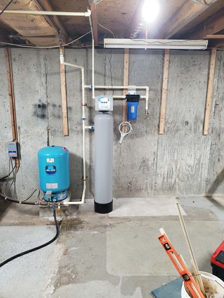 Water filtration system in a basement. Includes a blue pressure tank, gray water softener, and a blue filter.