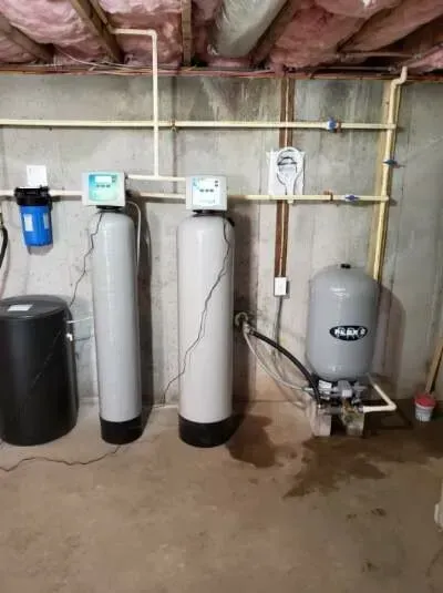 Basement water treatment system: filter, two tanks, pressure tank, pipes, and electrical components.