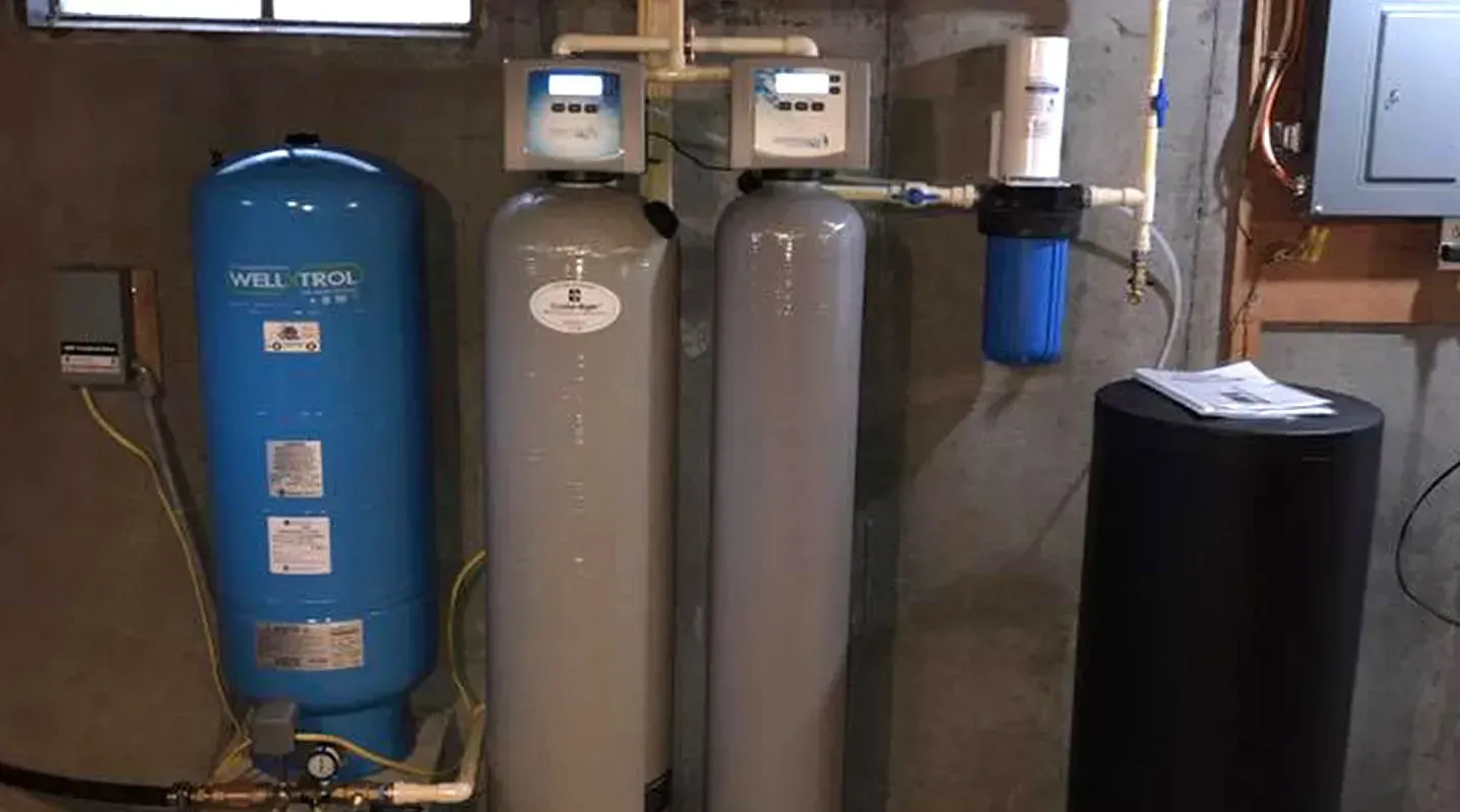 Water filtration system in a basement. Includes a blue tank, two gray tanks, and a blue filter.