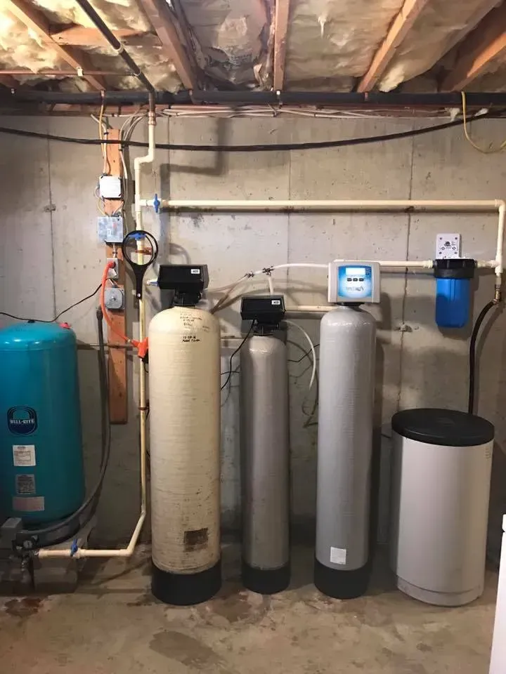Water filtration and treatment system in a basement. Includes a blue tank, several filters, and a salt tank.