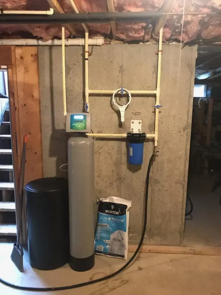 Water filtration system with tanks, filters, and piping against a concrete wall.