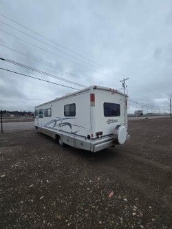 A white recreational vehicle parked on a gravel lot under a cloudy sky.