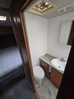 Interior of a camper bathroom featuring a white toilet, a wooden vanity with a sink, and a ceiling ventilation fan.