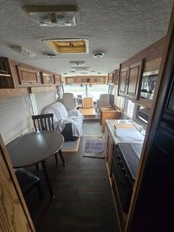 The interior of a recreational vehicle featuring a small dining table, a white-covered sofa, and wood-toned cabinetry.