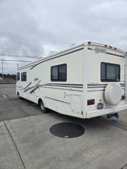 A white motorhome parked on a paved lot under a cloudy sky.