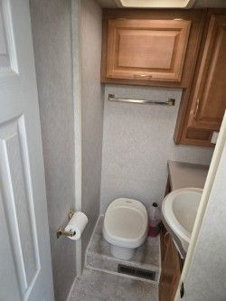 A small RV bathroom featuring a white toilet on a raised platform, a sink, and wooden cabinetry above a towel rack.