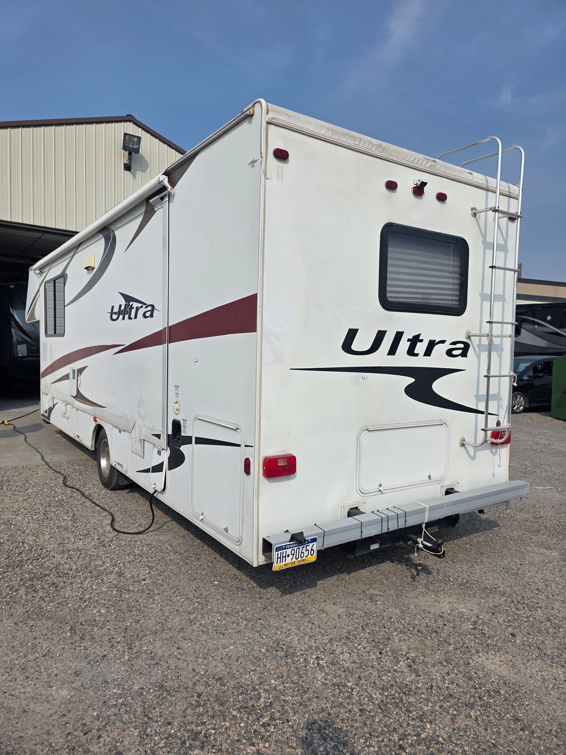White RV parked on gravel, showing rear and side.