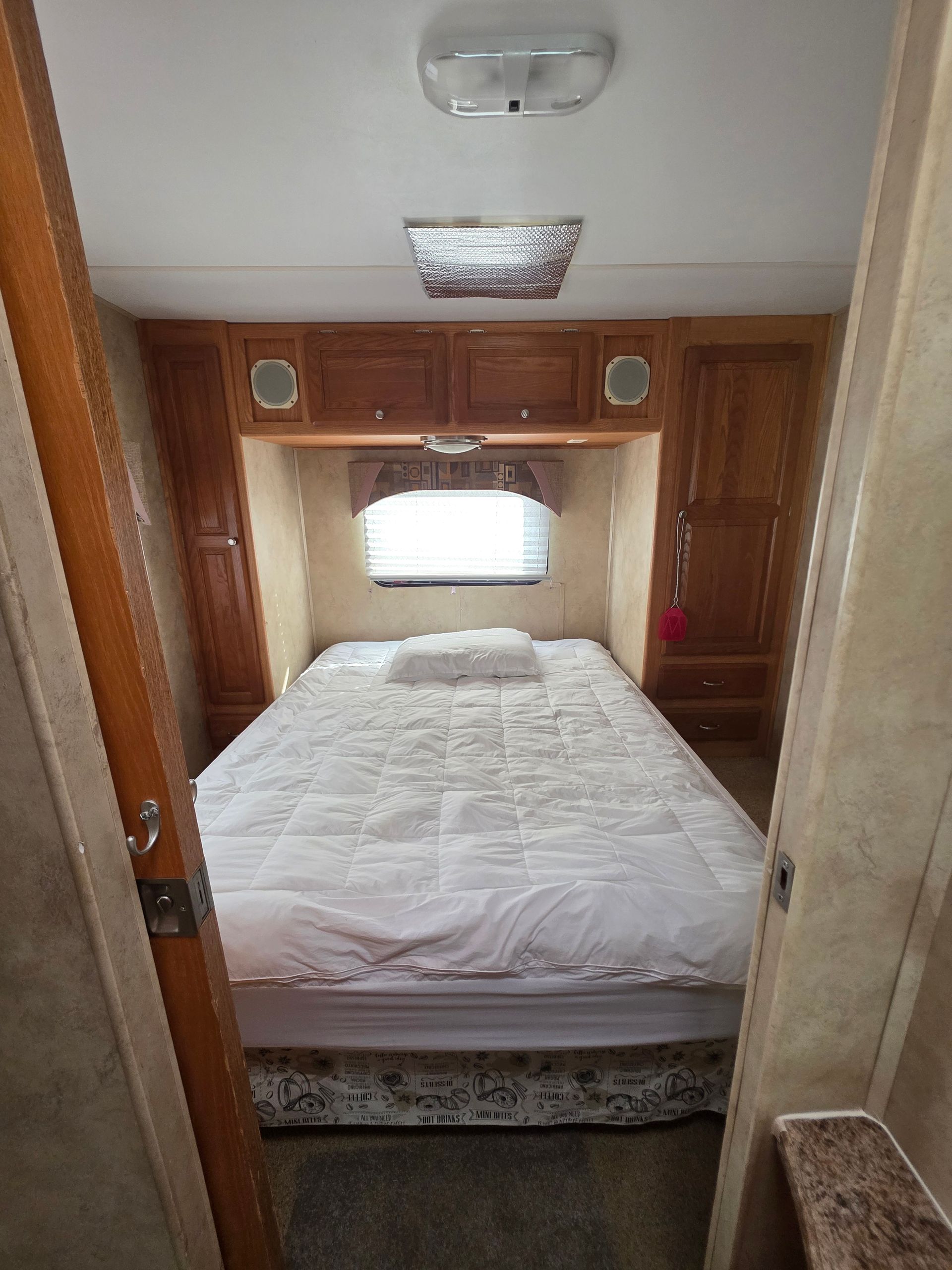 Bedroom in an RV with bed centered under cabinets.