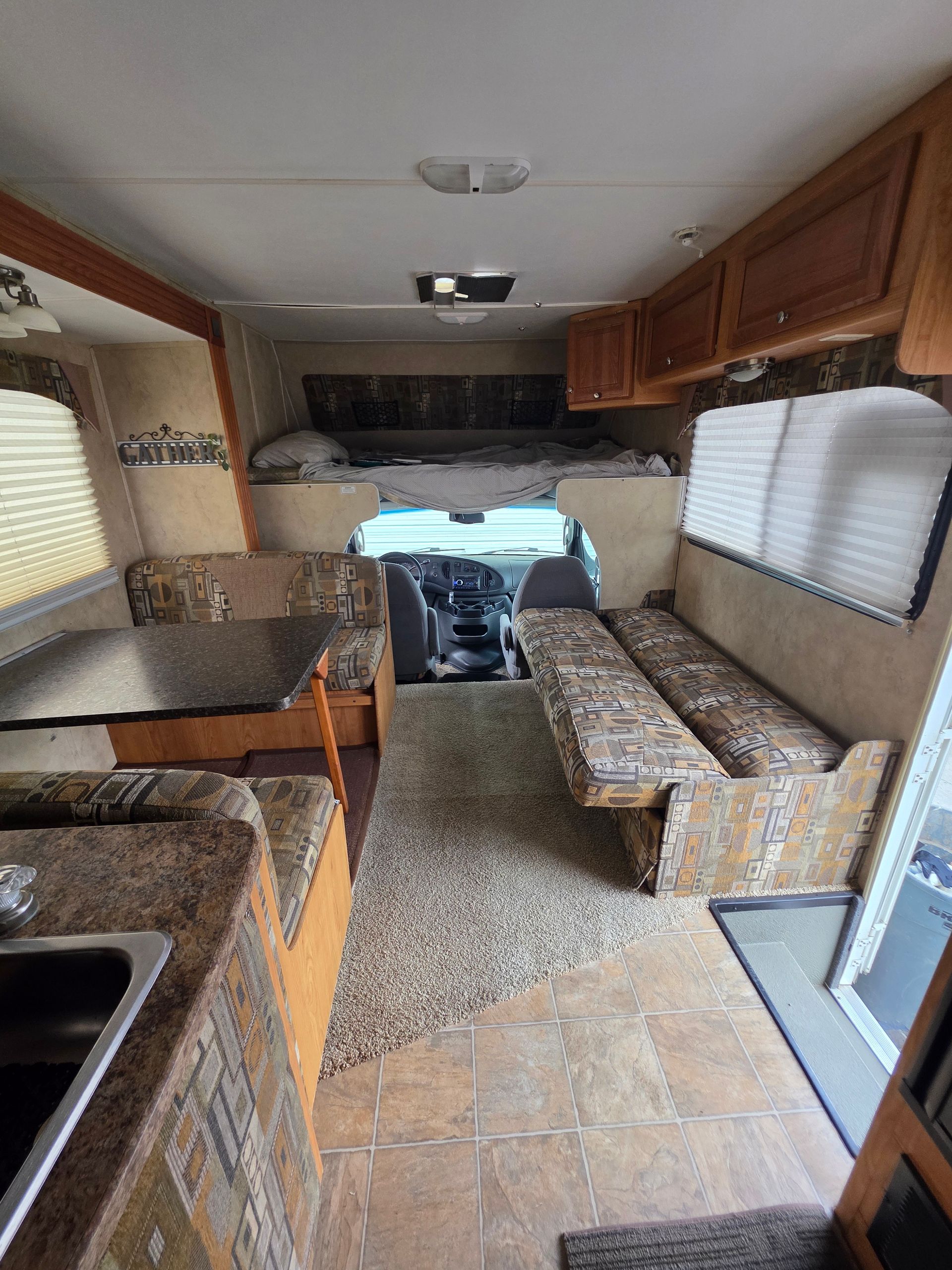 Interior view of an RV with a kitchen, dinette, and overhead sleeping area.