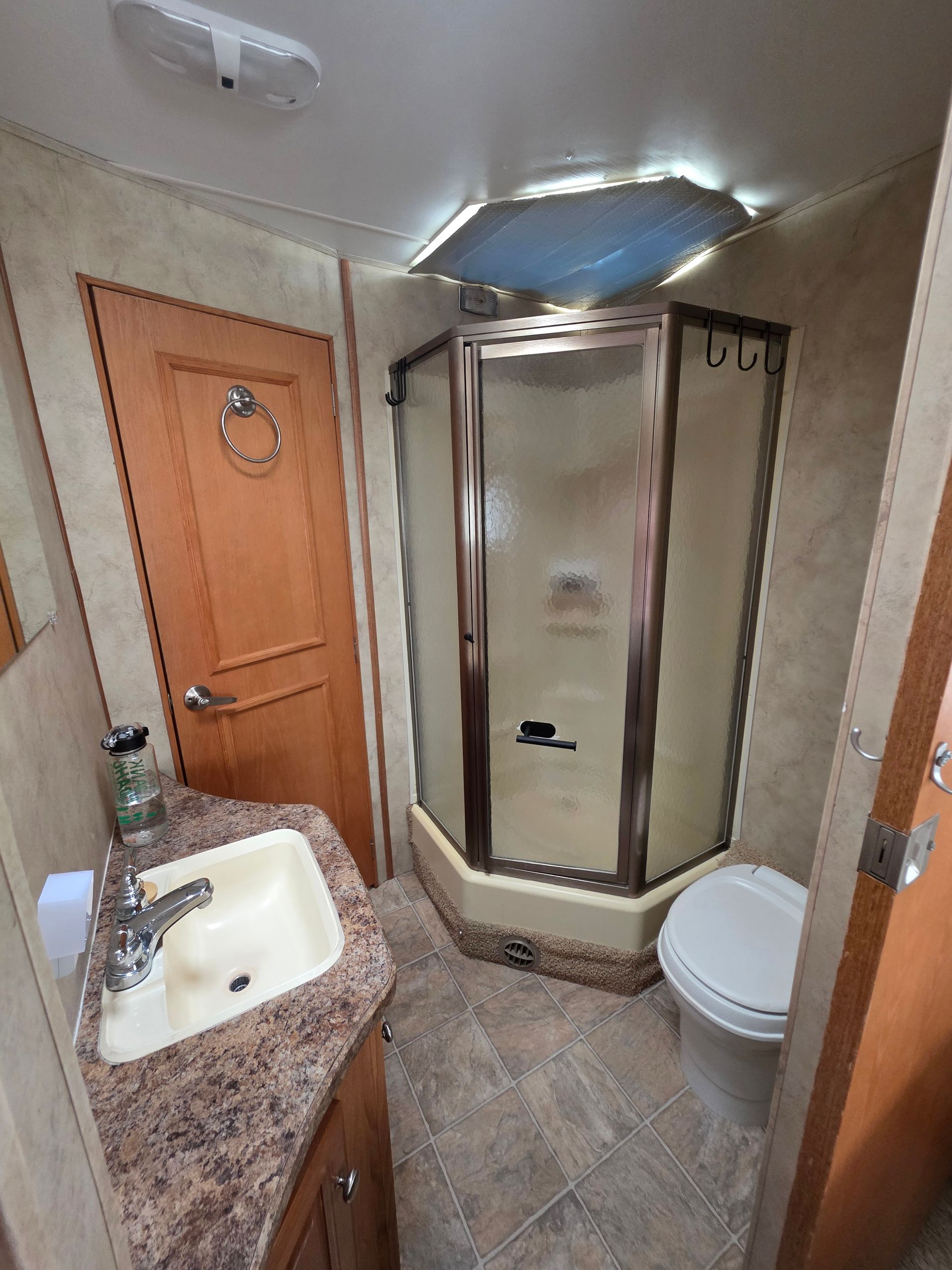RV bathroom with shower, toilet, sink, and closed door.