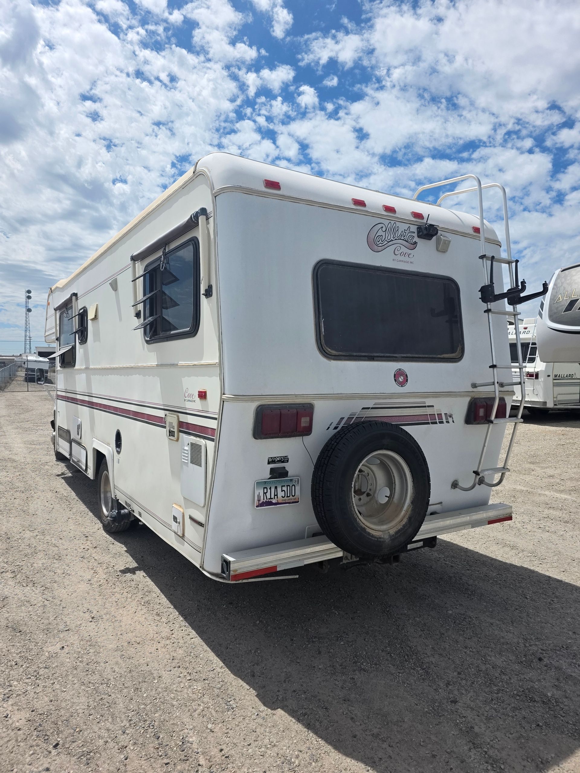 White RV parked on gravel under a cloudy blue sky.