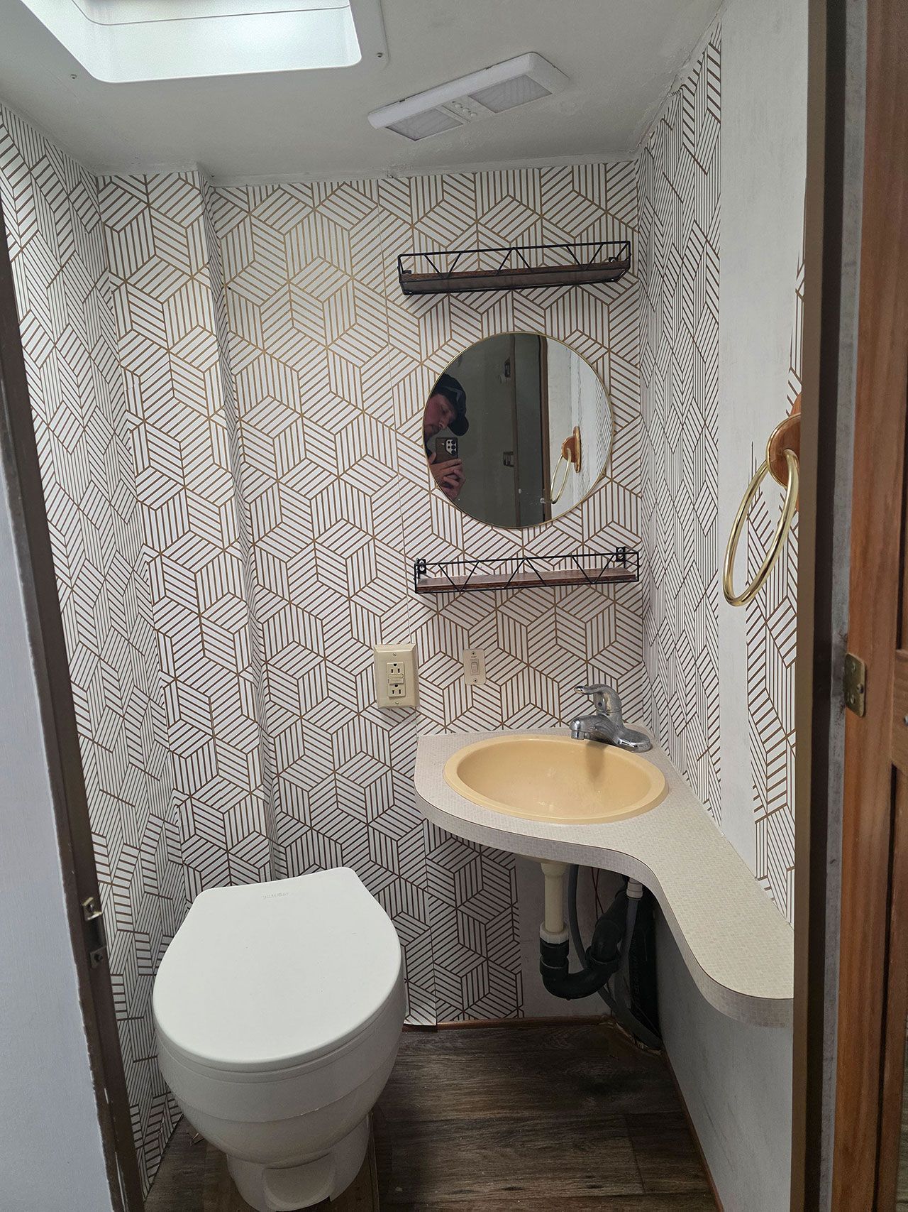 Small RV bathroom with patterned wallpaper, toilet, sink, and round mirror.