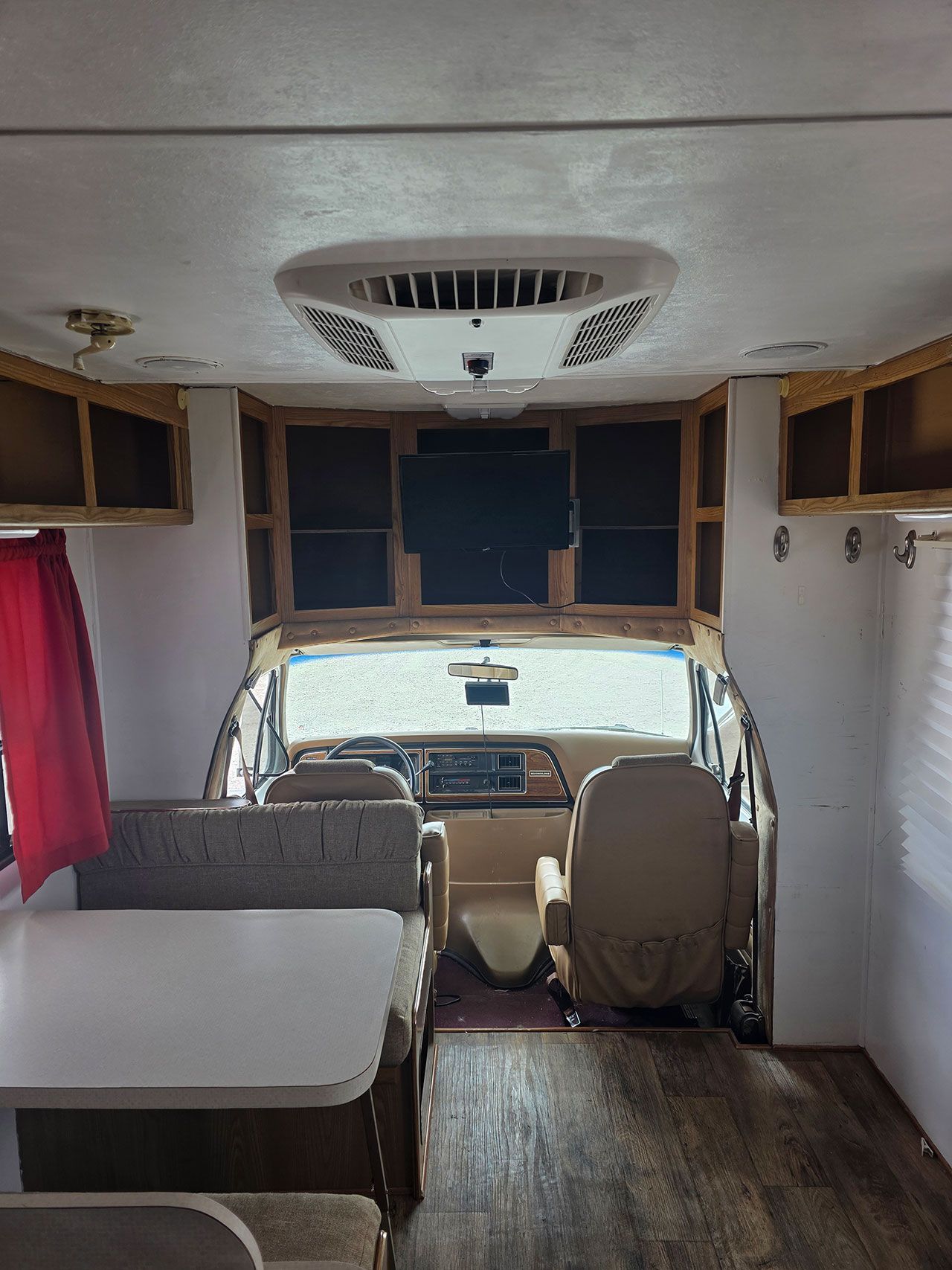 Interior view of a motorhome with cabinets, driver's seat, table, and air conditioning unit.