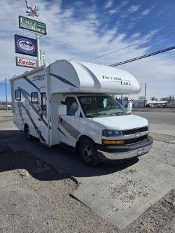 A white Sunseeker Class C motorhome parked on an asphalt lot near a roadside business sign under a blue sky.