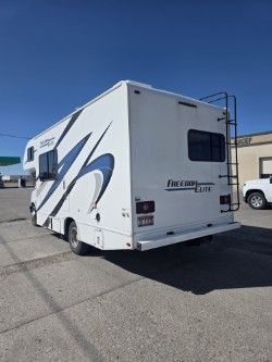 A white Freedom Elite motorhome with blue and black graphics parked on an asphalt lot under a clear blue sky.