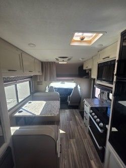 Interior view of an RV cabin showing a dinette, a small kitchen with a stove, and the driver's area at the front.