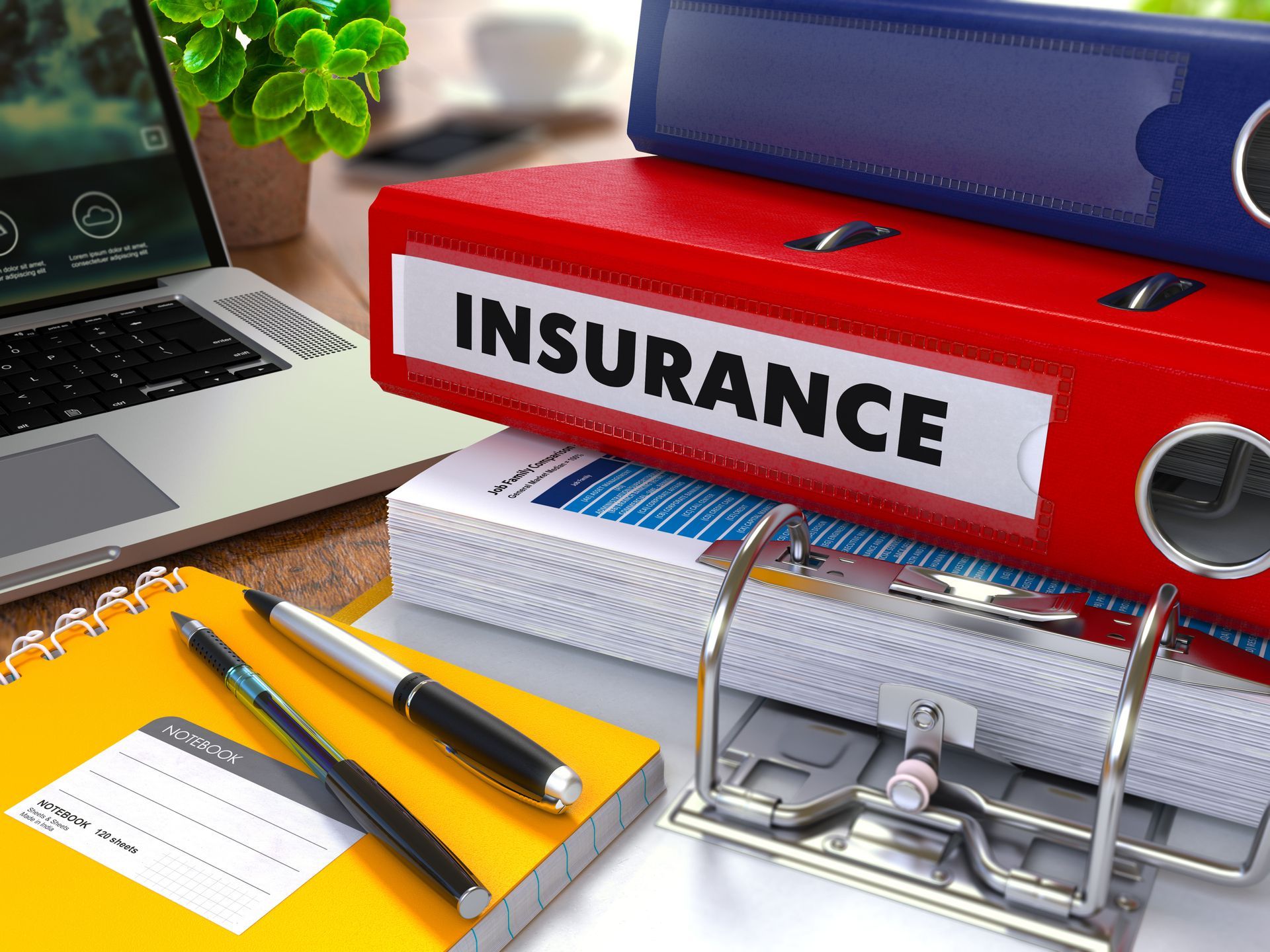Insurance binders and office supplies beside a laptop on a desk