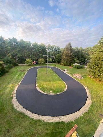 An aerial view of a newly paved driveway surrounded by grass and trees.