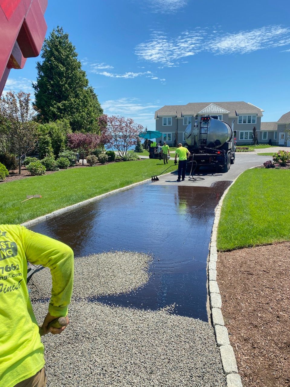 A man in a yellow shirt is standing next to a truck that is painting a driveway.
