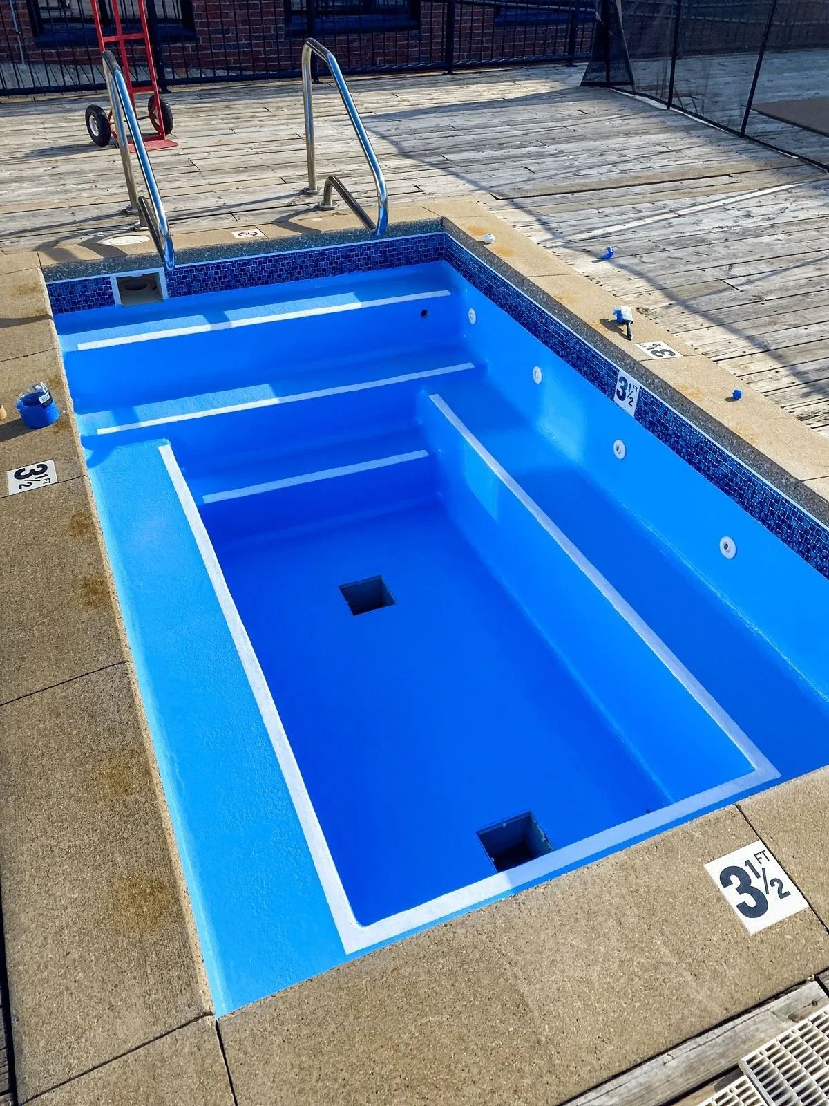 Empty blue pool with tiled trim and depth markers. Handrails and steps are visible.