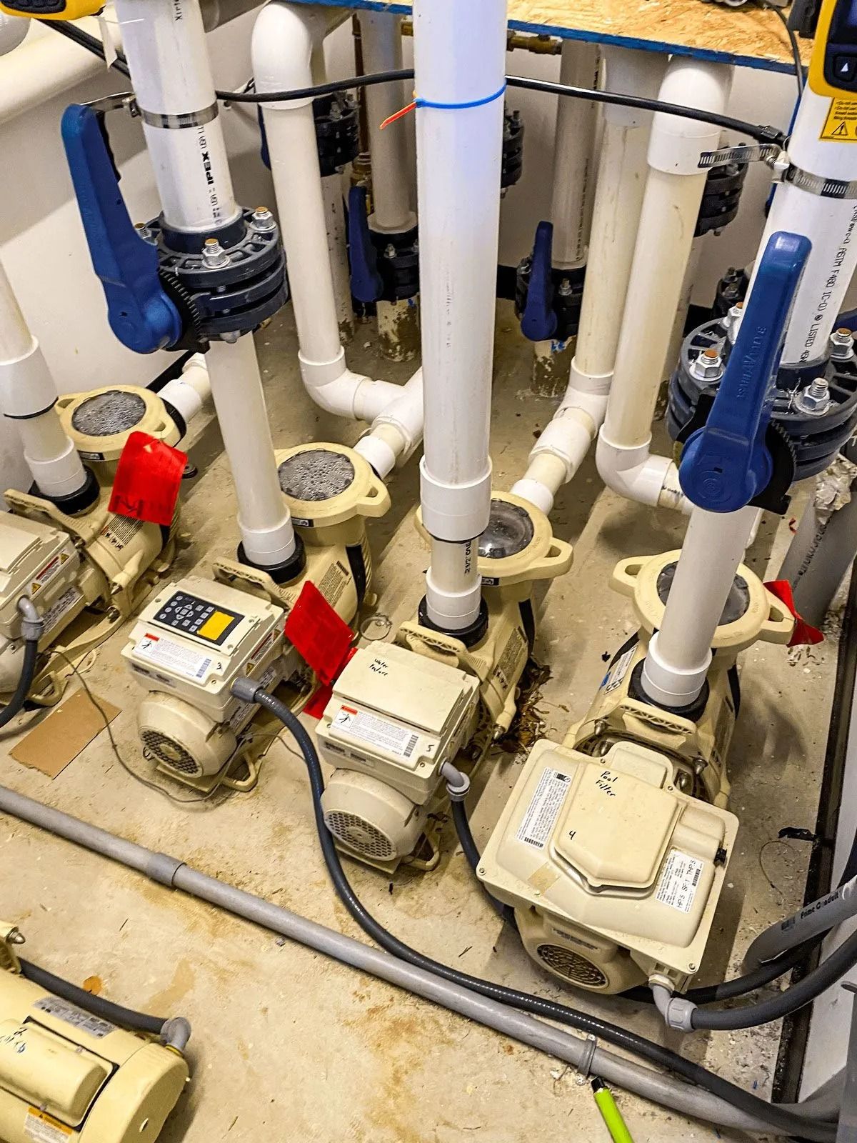 Pool pump system with beige pumps and white pipes, blue handles, and gray cords.