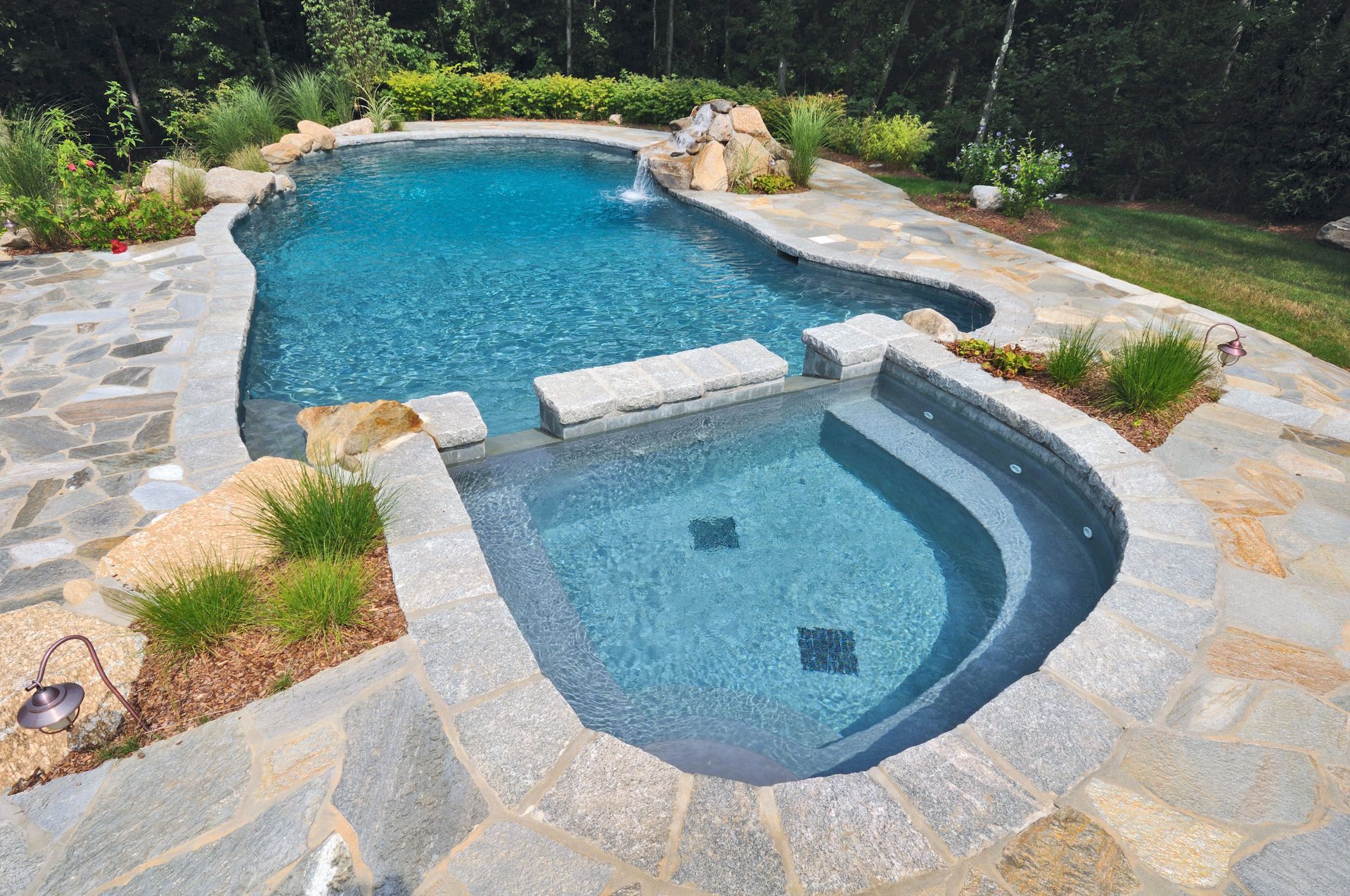 Freeform swimming pool and spa with flagstone surround; blue water, stone accents, and greenery.