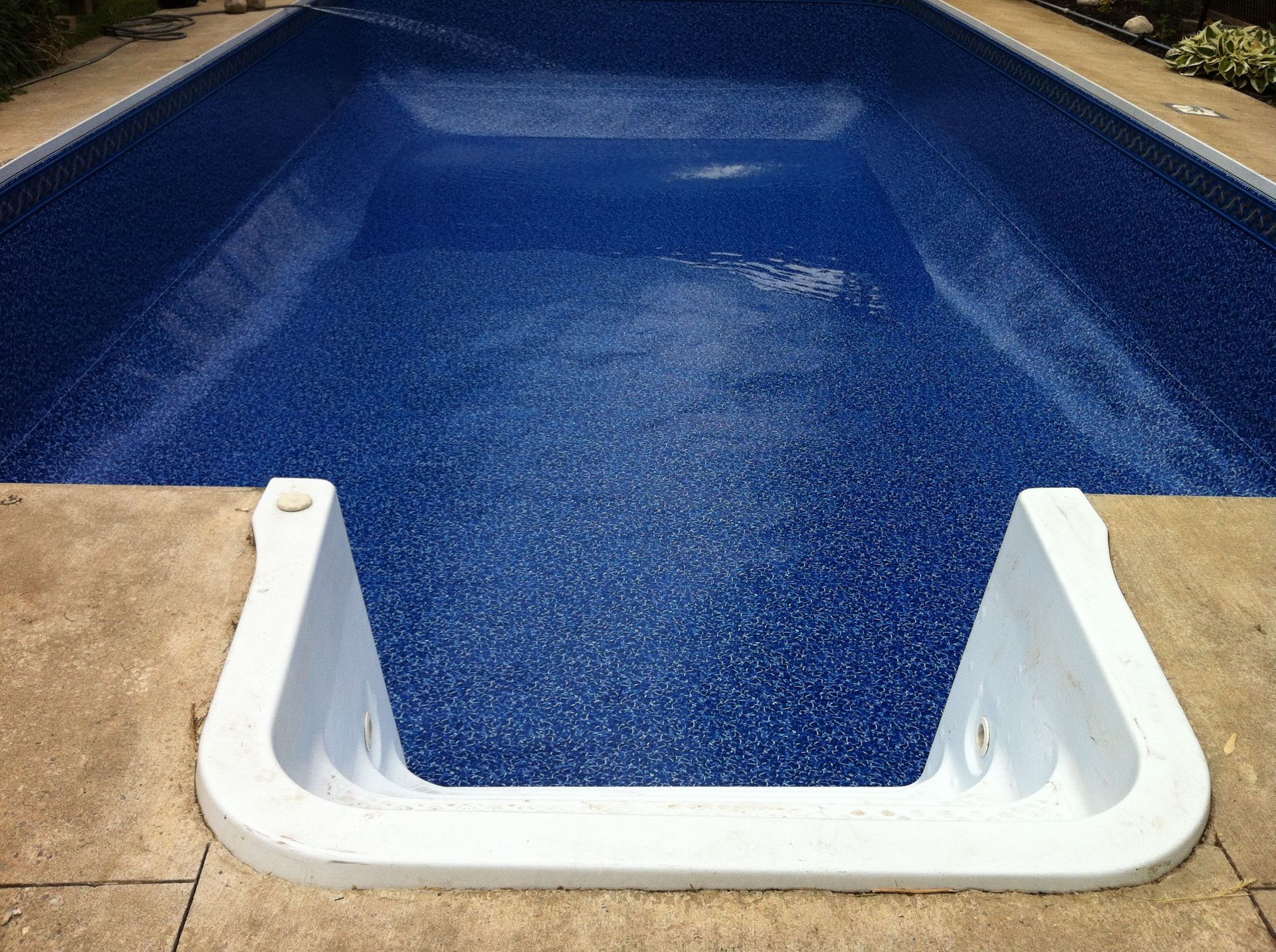 Empty blue speckled swimming pool with white steps, surrounded by concrete.