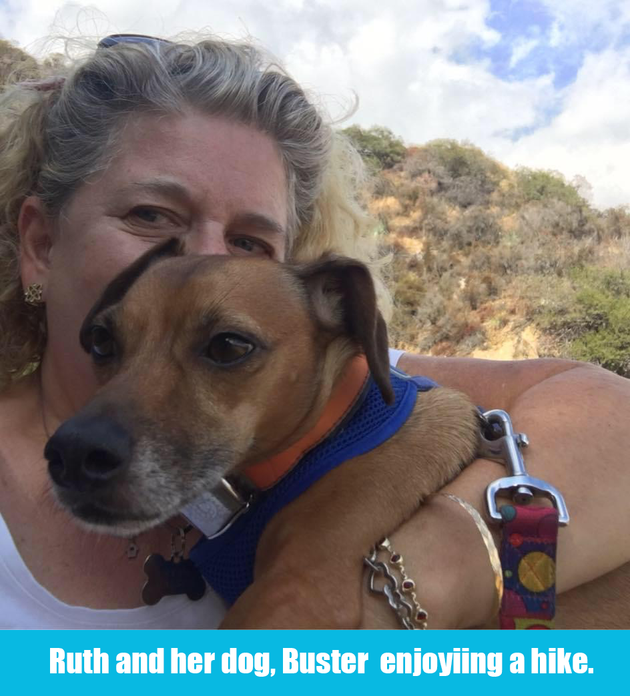Woman holds a brown dog on a hike, with hills and cloudy sky in the background.