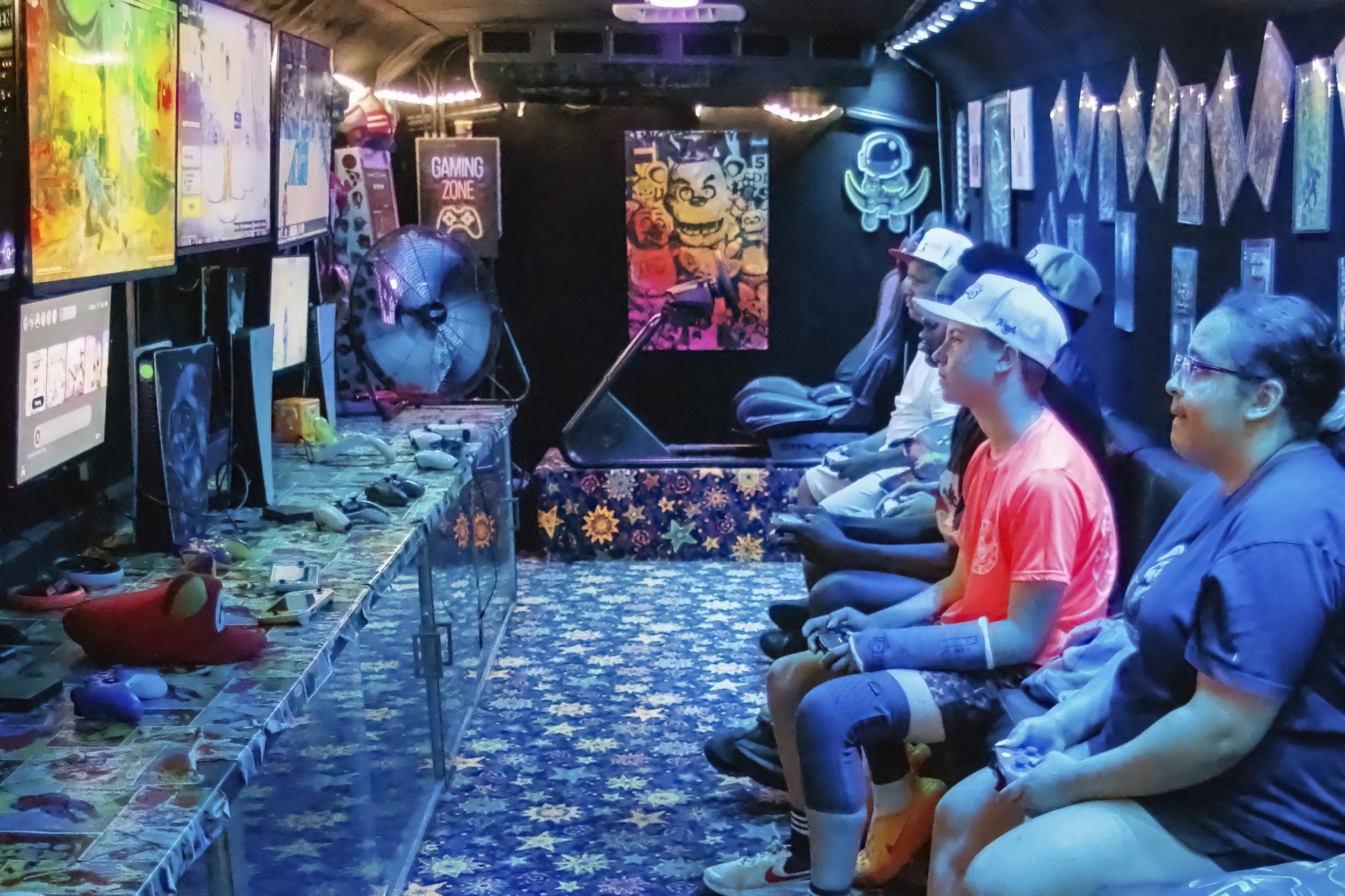 People seated in a colorful VR arcade, wearing headsets and holding controllers, with neon-lit walls and screens.